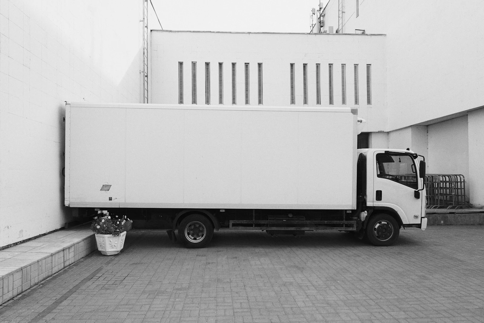 Unmarked white box truck parked beside a building, in black and white
