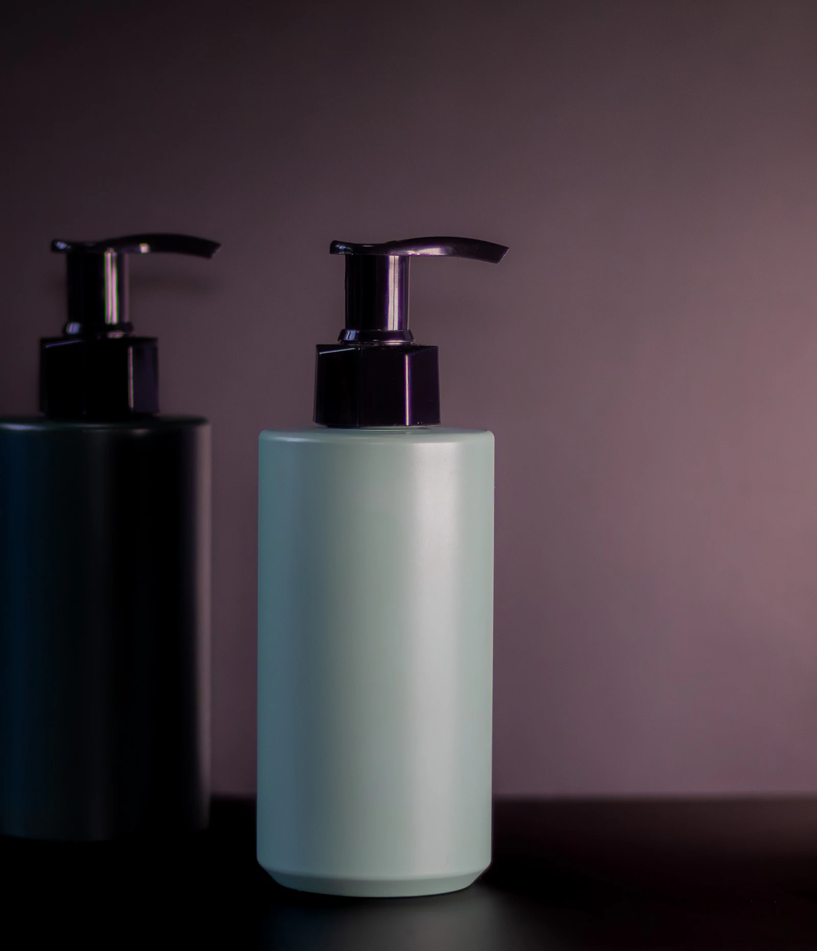Two unlabeled pump bottles for soap or lotion on a dark shelf