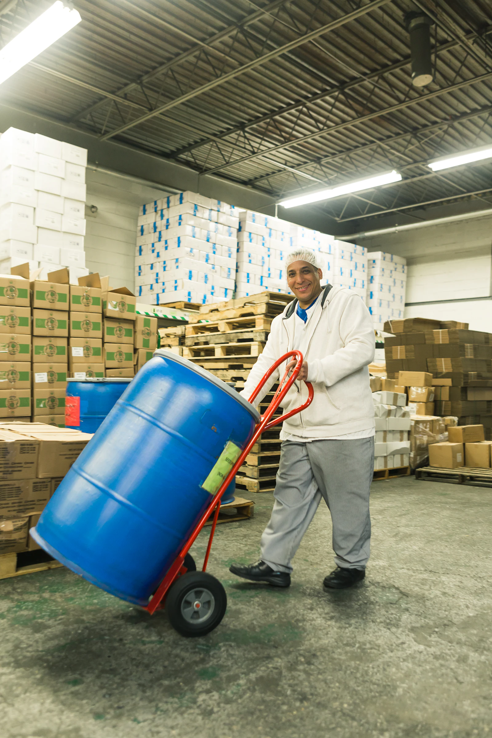 Warehouse worker moving a plastic drum on a hand truck past stacked cases
