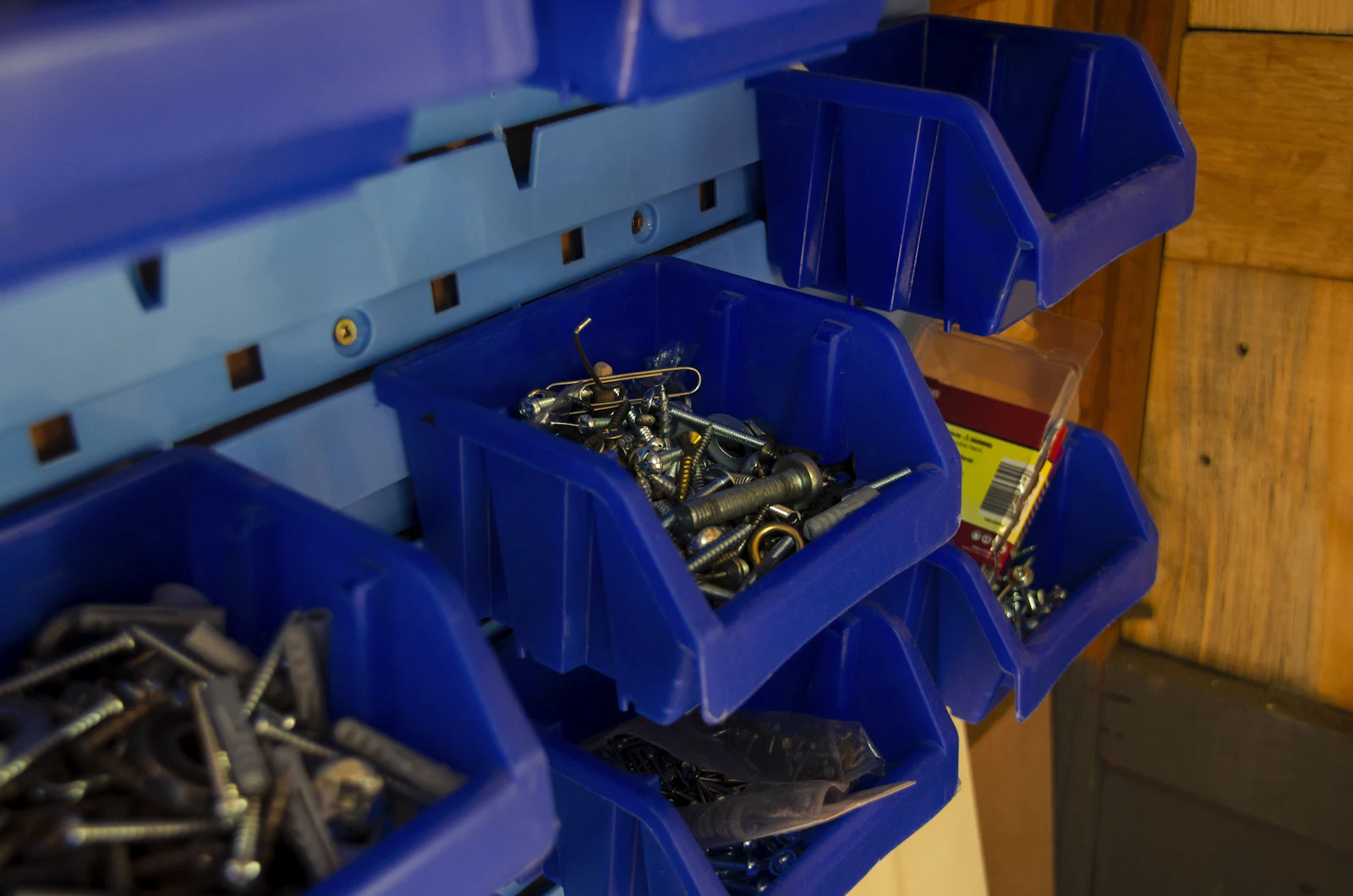 Blue parts bins on a wall rack filled with screws, hooks, and anchors