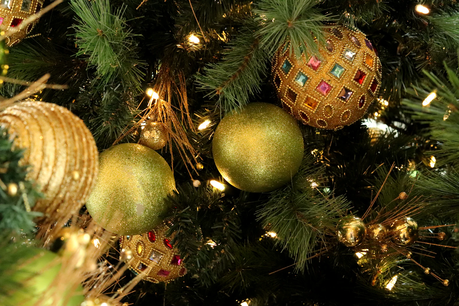 Gold and glitter ornaments on a lit holiday tree