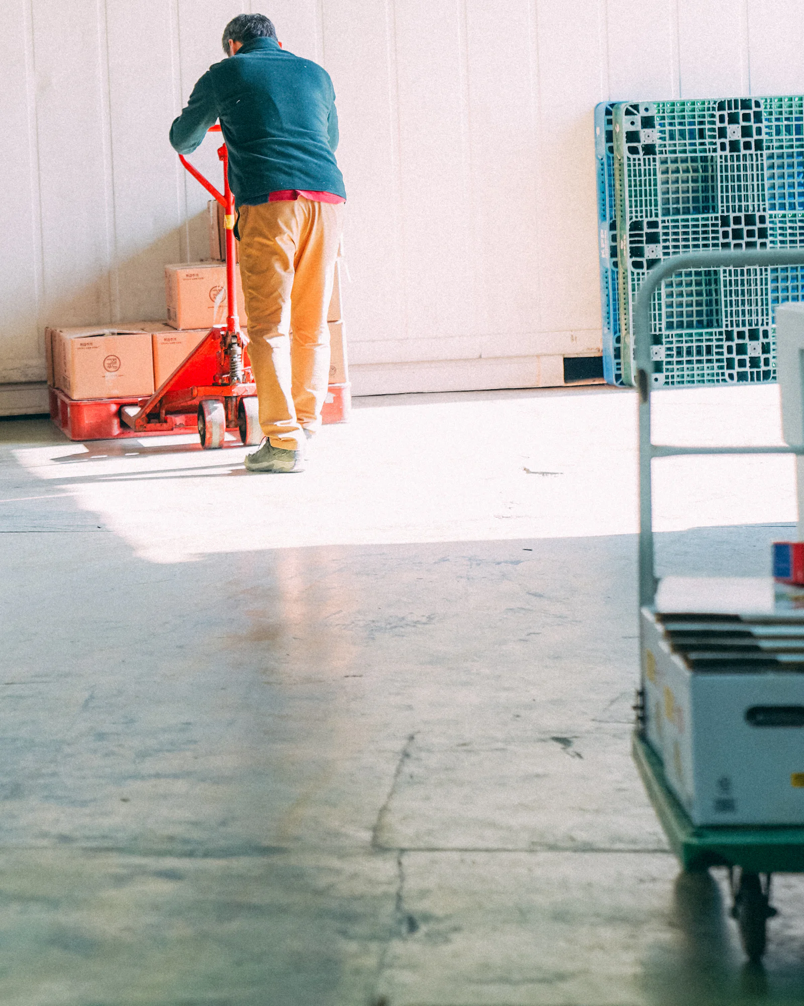 Worker moving cases on a manual pallet jack inside a warehouse