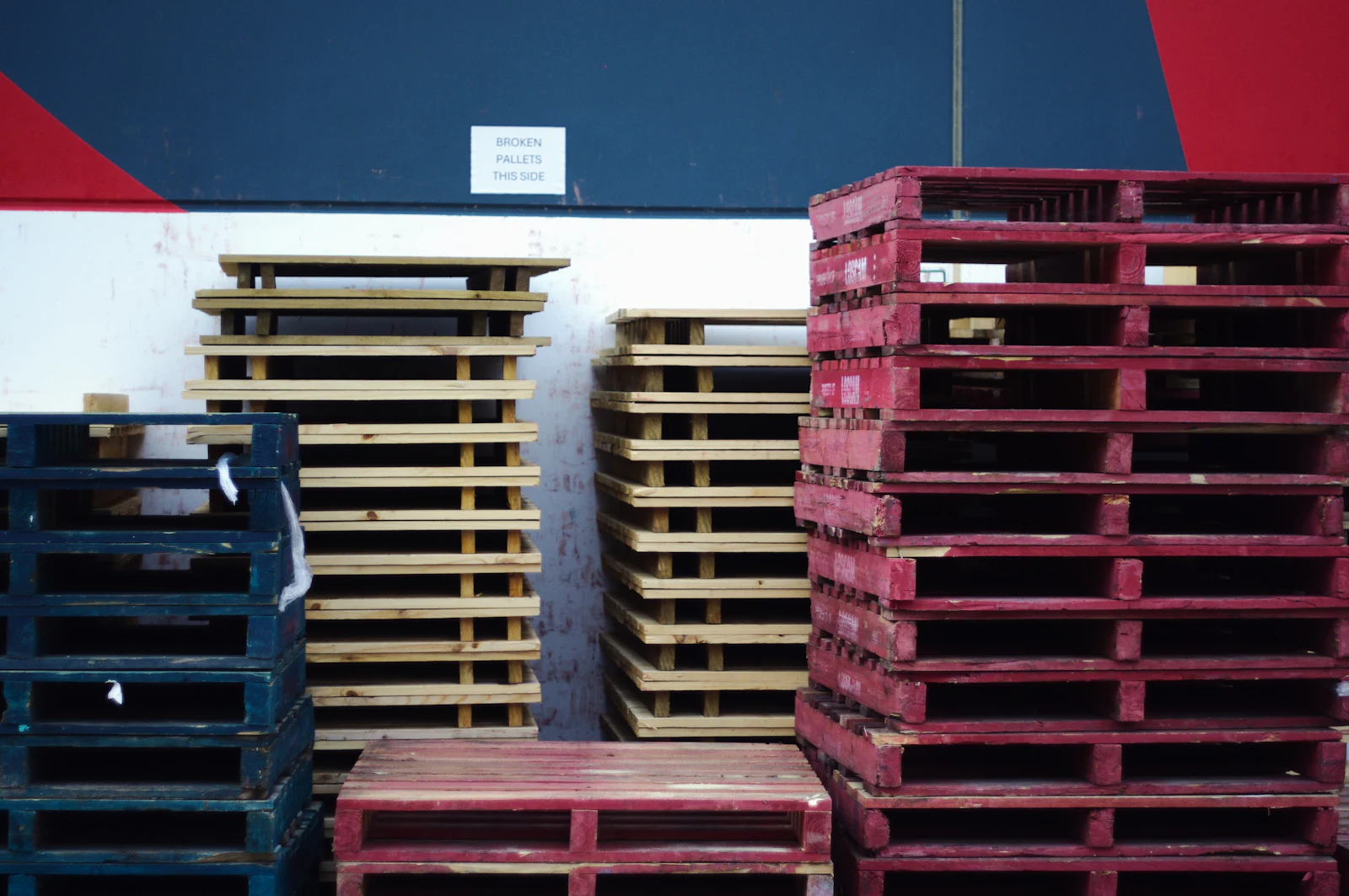Stacks of painted wooden pallets below a sign for broken pallets