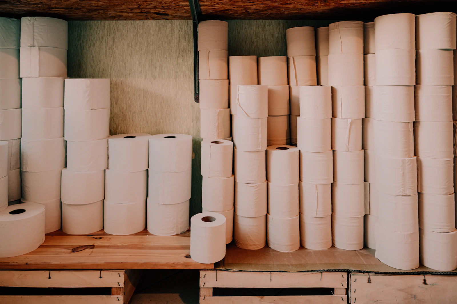 Rolls of toilet paper and paper towels stacked on wooden shelves