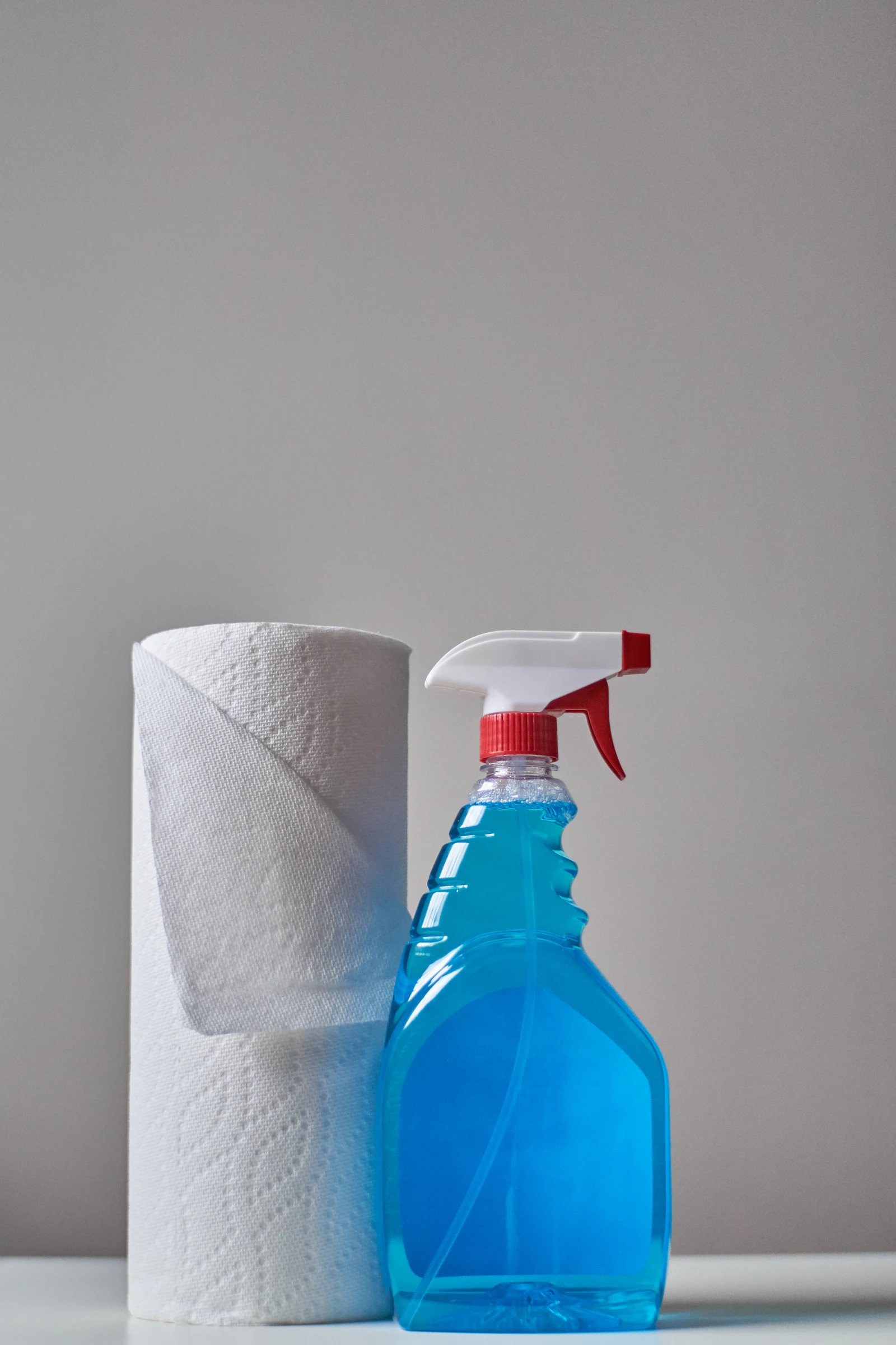 Paper towel roll standing next to a blue spray bottle of cleaner